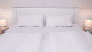 A neatly made bed with white linens and pillows, two bedside lamps, and a plain wall. - Apartment Stark by Interhome (Norddeich)