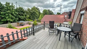 A wooden deck with a table and chairs, surrounded by a brick wall and a metal fence. - Apartment Stark by Interhome (Norddeich)