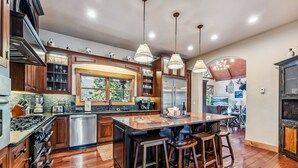 A spacious kitchen with wooden cabinets, stainless steel appliances, and a large island with stools. - Luxurious 5BDR Getaway w/ Hot Tub & Mountain Views (Blue River)