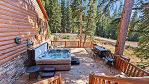 A wooden deck with a hot tub, outdoor furniture, and a view of a forest. - Luxurious 5BDR Getaway w/ Hot Tub & Mountain Views (Blue River)