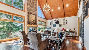 A spacious living room with wooden floors, large windows, and a high ceiling. - Luxurious 5BDR Getaway w/ Hot Tub & Mountain Views (Blue River)