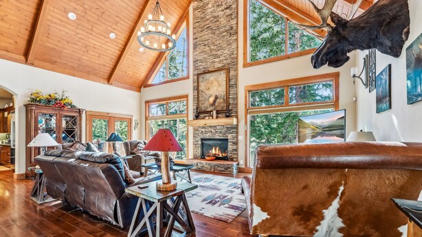 A spacious living room with a stone fireplace, leather furniture, and a mounted moose head. - Luxurious 5BDR Getaway w/ Hot Tub & Mountain Views (Blue River)