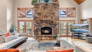 A spacious living room with a stone fireplace, a large flat-screen TV, and a comfortable seating area with sofas and a coffee table. - Stunning 6BR Lodge w/ Beautiful Mt. Quandary Views (Blue river)