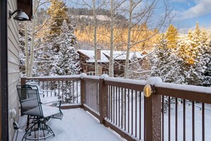 A snow-covered deck with a chair and a railing, overlooking a forested area with snow-covered trees and buildings. - Expansive Retreat with Hot Tub and Game Room (Breckenridge)