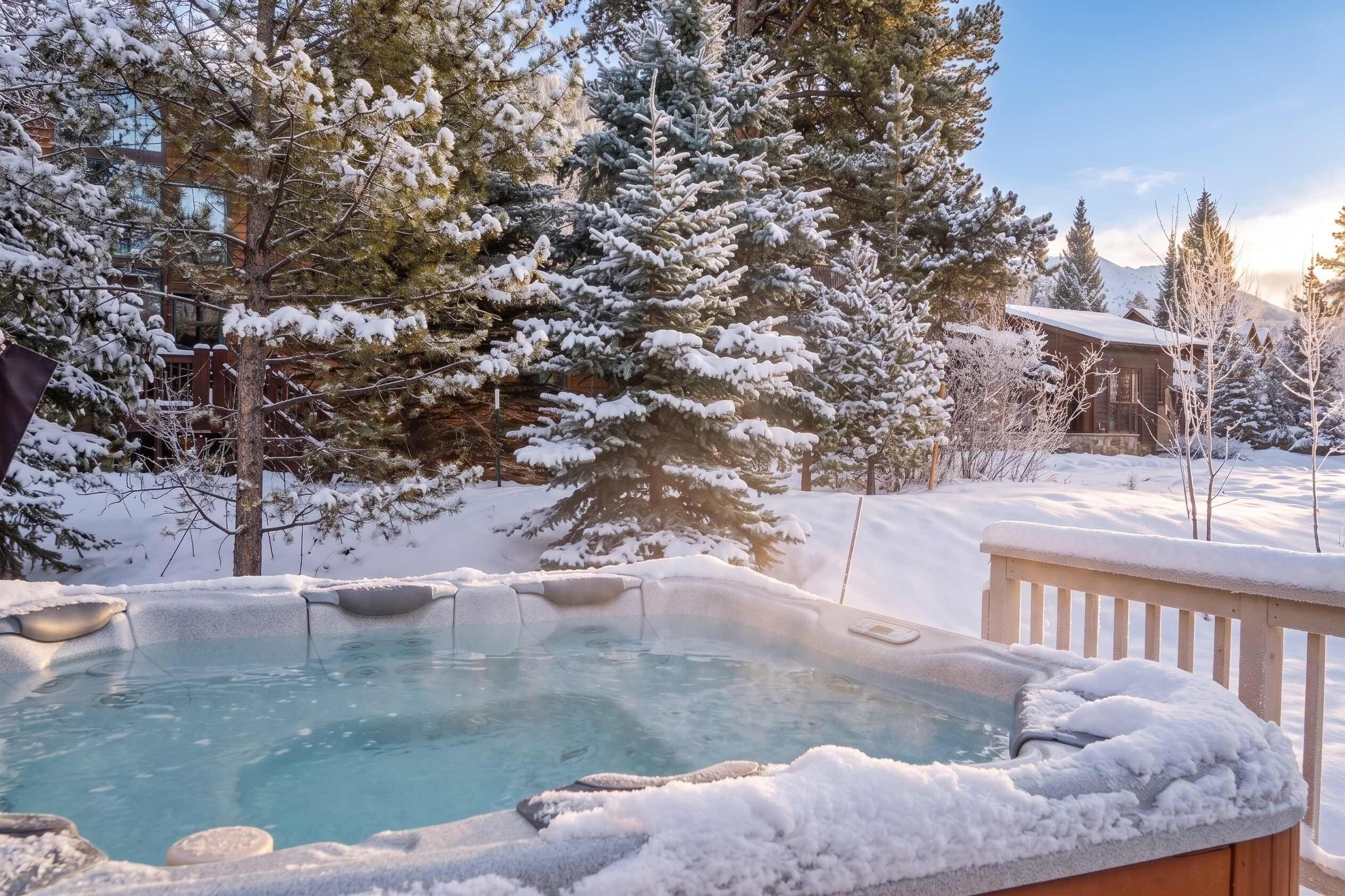 Un bain à remous entouré d’arbres couverts de neige, avec un bâtiment en arrière-plan.