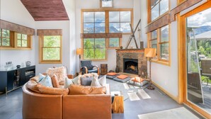 Un salon spacieux doté d’une cheminée, de grandes fenêtres offrant une vue sur les montagnes et d’un coin salon confortable.