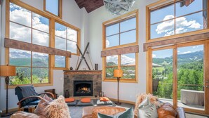 Un salon spacieux avec des canapés en cuir, une cheminée en pierre et de grandes fenêtres offrant une vue sur les montagnes.