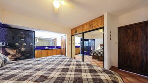 A bedroom with a checkered bedspread, wooden cabinets, a mirrored closet door, and a bathroom visible through an open door. - A-609 Vacation in this Exquisite Spacious 2-bedroom condominium! (Cabo San Lucas)