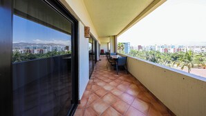 A balcony with a tiled floor, a table and chairs, and a view of a cityscape with buildings and palm trees. - A-609 Vacation in this Exquisite Spacious 2-bedroom condominium! (Cabo San Lucas)