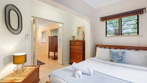 Hotelkamer met een bed, een dressoir, een lamp, een spiegel en een raam met jaloezieën.