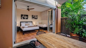 Een slaapkamer met een bed, een plafondventilator en een schuifglazen deur naar een balkon met een tafel en stoelen.