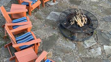Un hogar con fuego rodeado por seis sillas Adirondack con cojines a rayas azules, dispuestas en un patio de piedra.