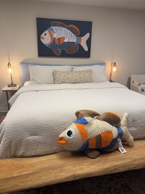 A bed with a plush fish toy, a patterned pillow, and a painting of a fish on the wall.