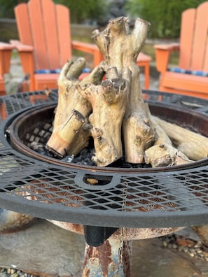 A metal fire pit with logs, surrounded by orange chairs.