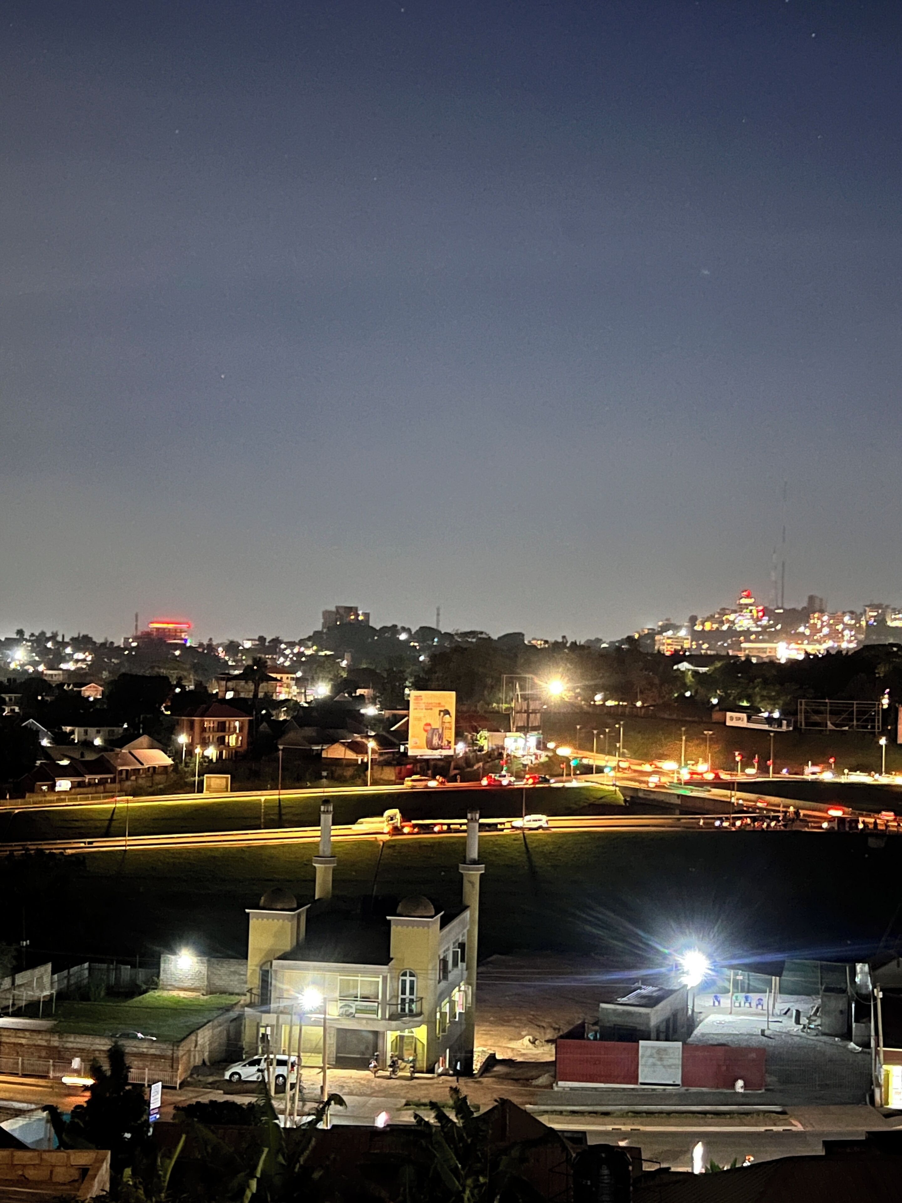 A nighttime view of a cityscape with illuminated buildings and a highway with moving vehicles.