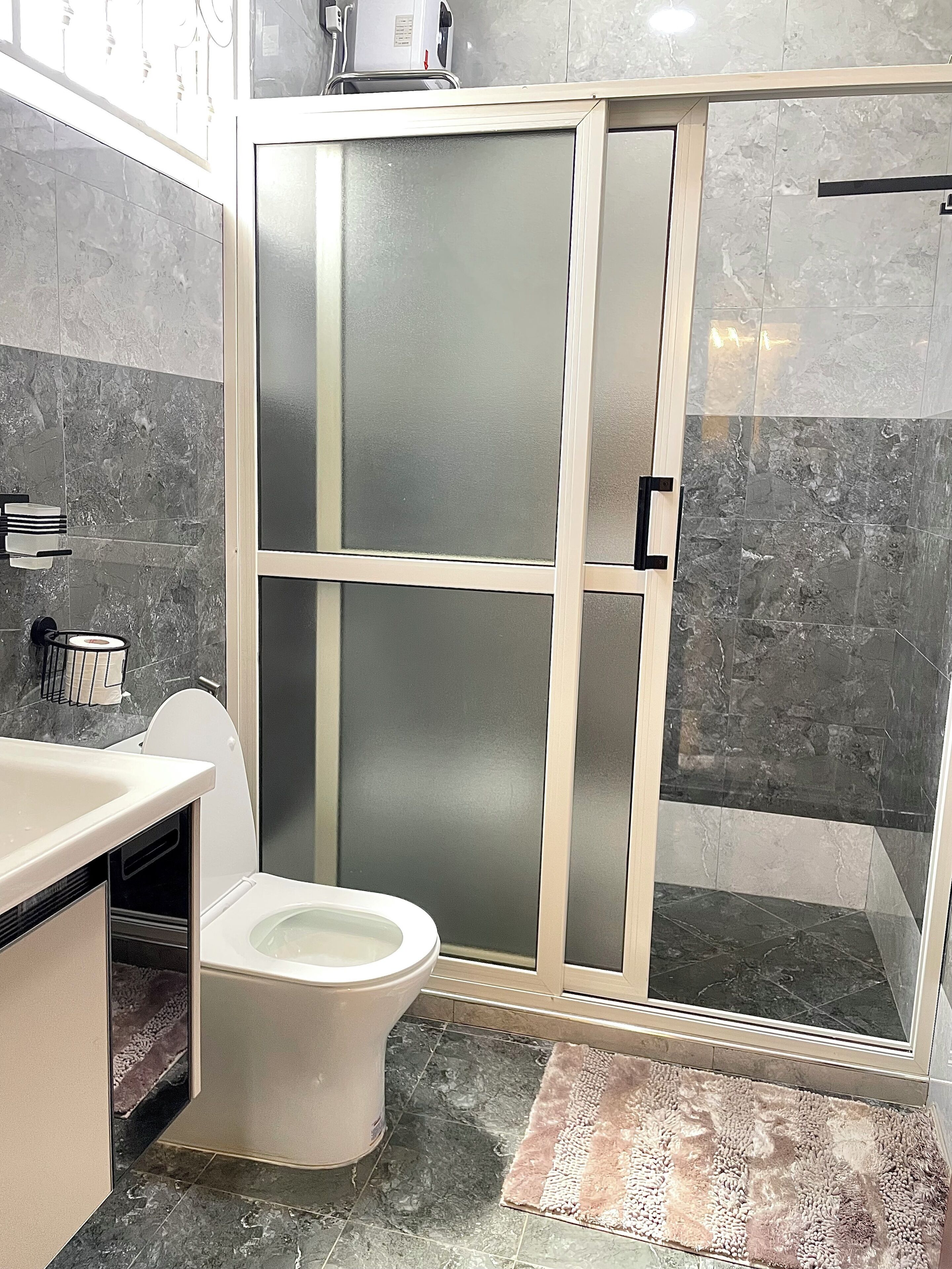 A bathroom with a toilet, a sink, a shower enclosure, and a marble-tiled floor.