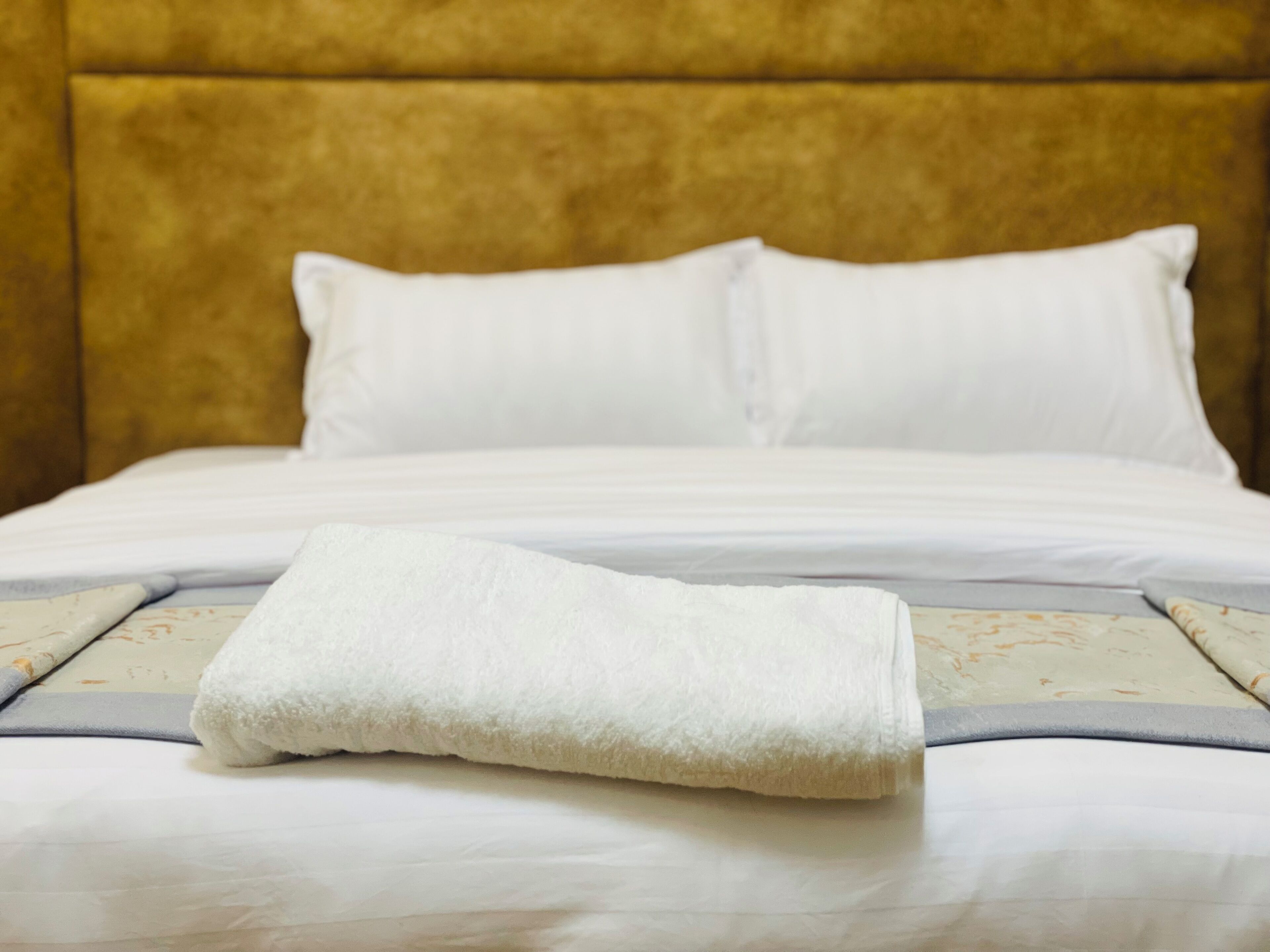 A neatly made bed with white linens and a folded white towel on top.