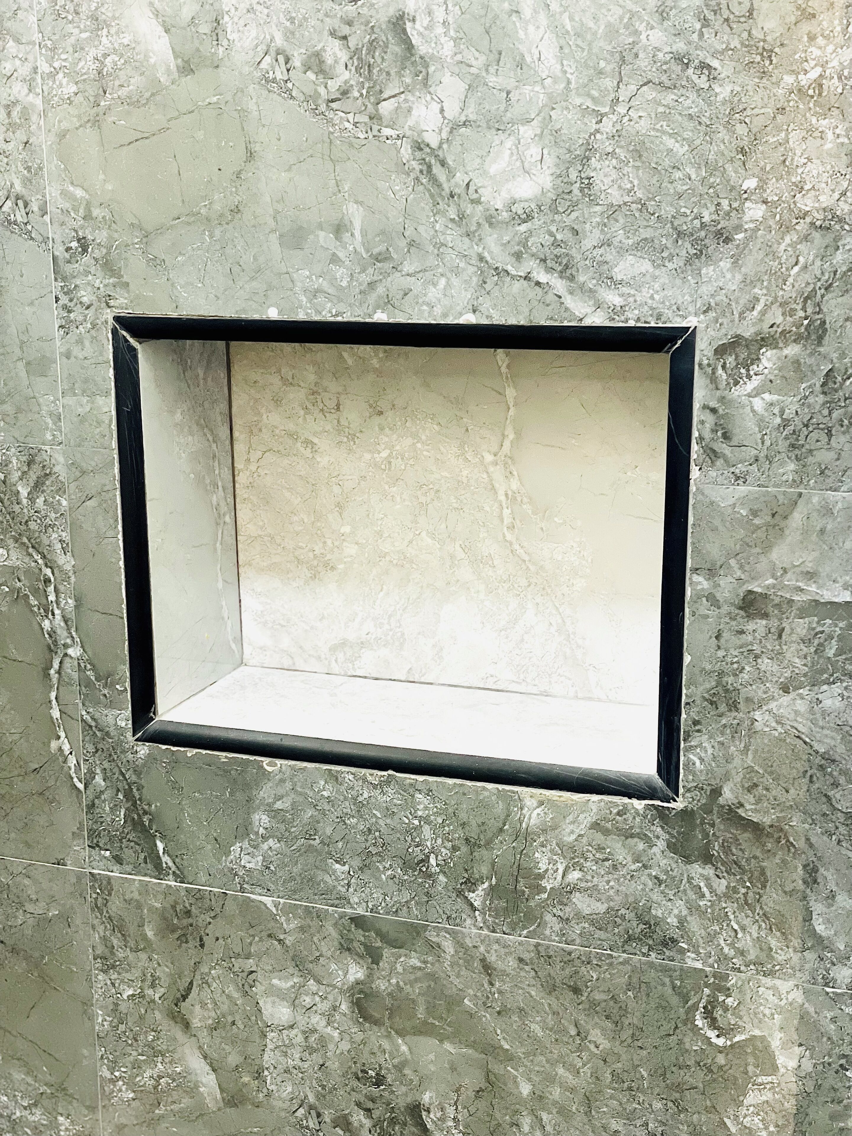 A rectangular, empty wall-mounted frame with a black border, set against a textured, marble-like wall.