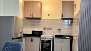 A modern kitchen with a built-in oven, microwave, and a dining area with a blue chair. - Lee Villas  (Kampala)