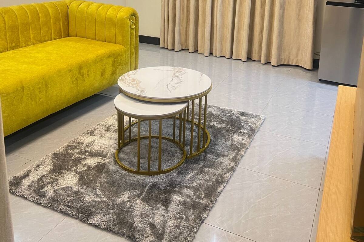 A modern living room with a yellow sofa, a round table with a marble top, and a grey shag rug.