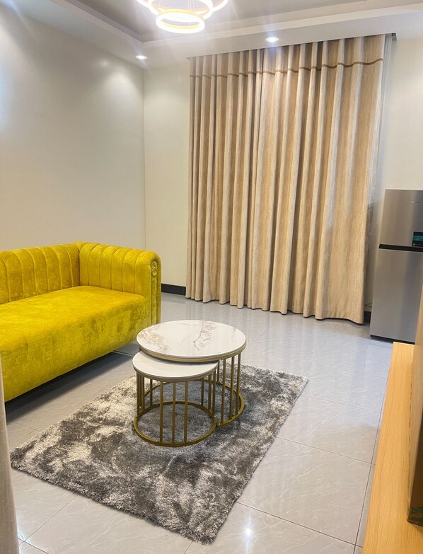Una sala de estar moderna con un sofá amarillo, una mesa redonda con cubierta de mármol y una alfombra mullida gris.