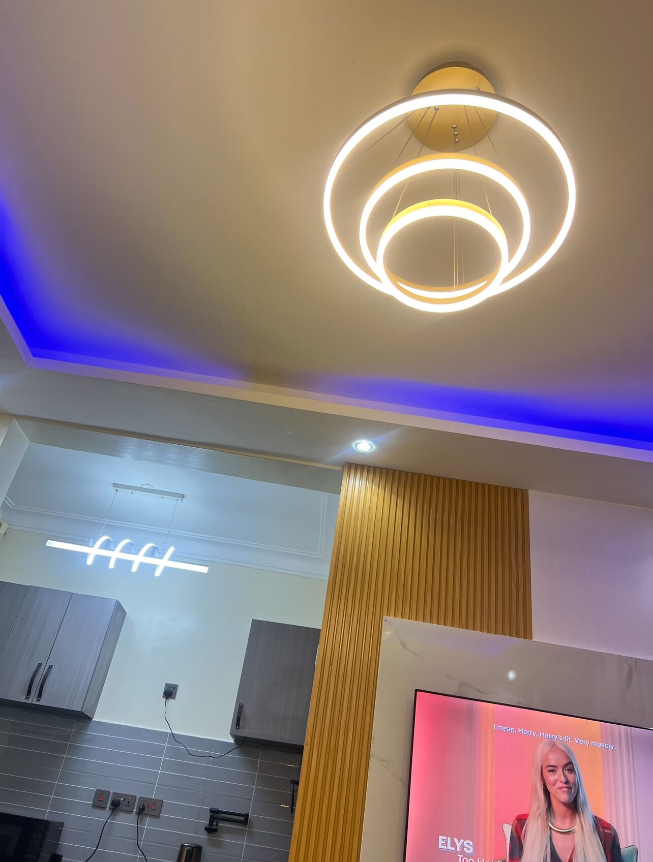 A modern interior with a circular light fixture, a wall-mounted sign, and a television screen displaying a movie title.