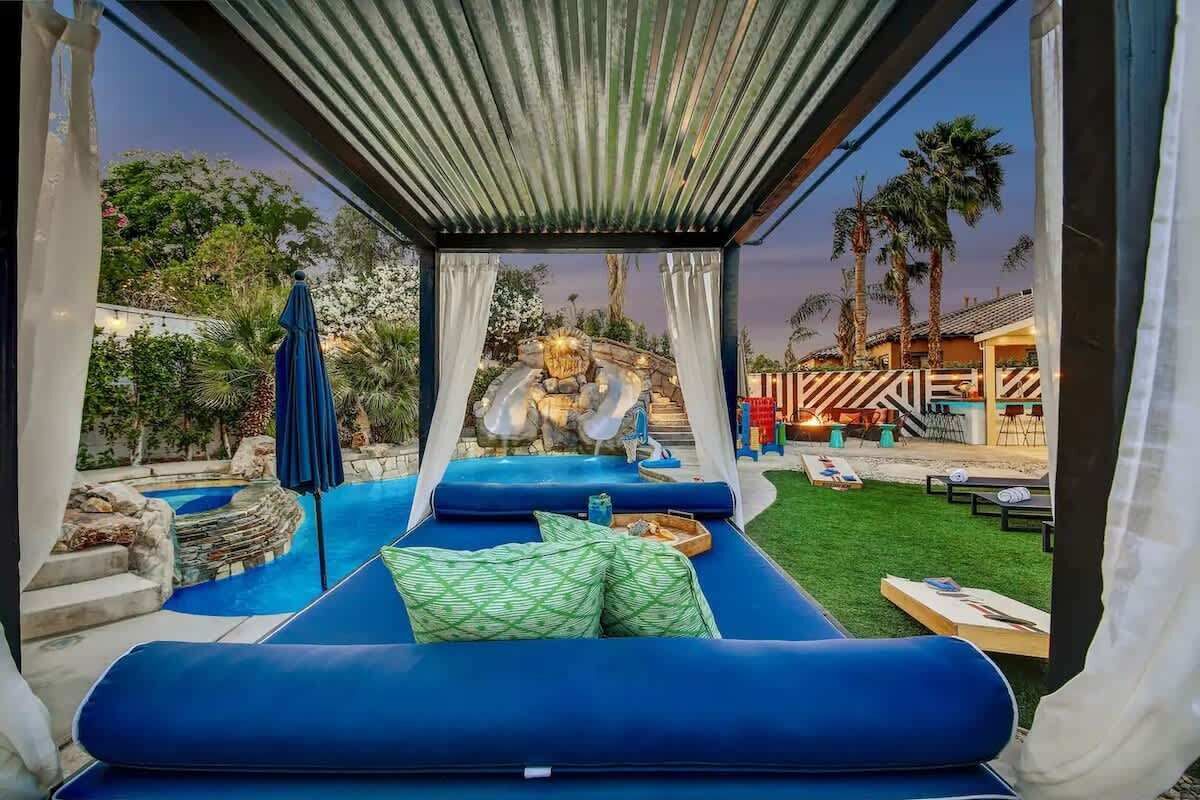 Zona de relax al costat d'una piscina, amb vista a una cascada, la piscina i un pati amb mobles d'exterior.