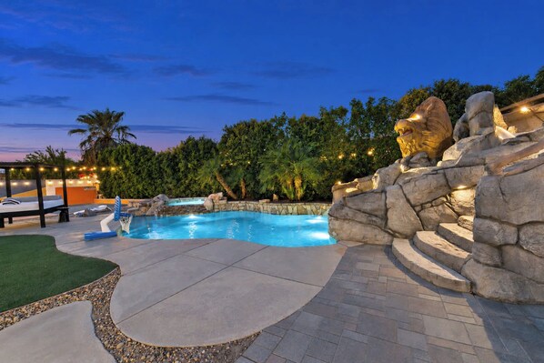 A swimming pool with a rock waterfall feature, surrounded by a stone wall and palm trees.