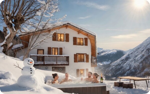 A chalet with a hot tub, surrounded by snow and mountains.