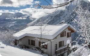 A snow-covered mountain house with a balcony and a view of the surrounding mountains.