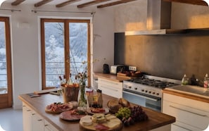 A kitchen with a central island, a stove, and a view of snow-covered trees through large windows.