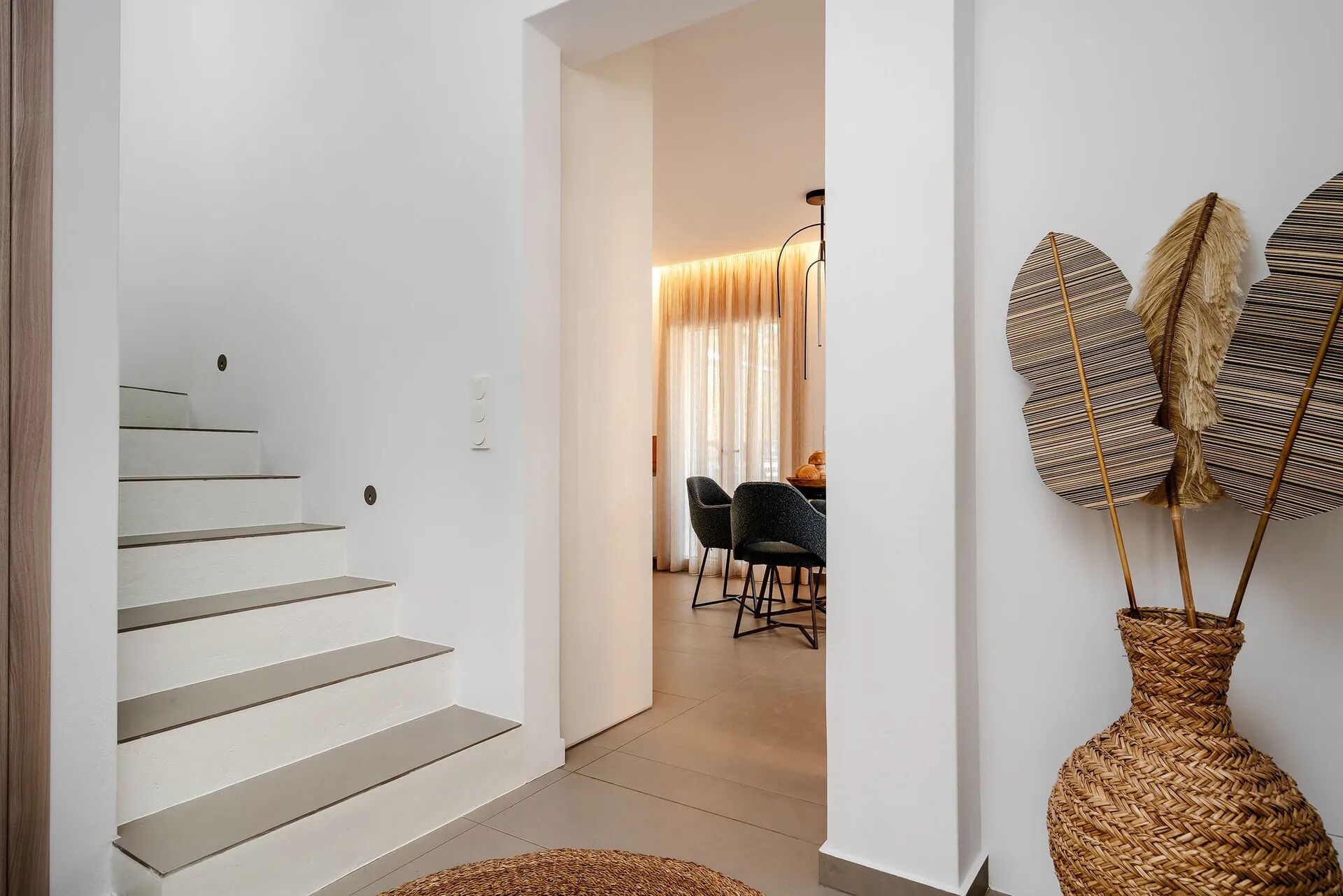 A staircase leading to a dining area with a table and chairs, a woven basket on the floor, and a wall-mounted decorative item.