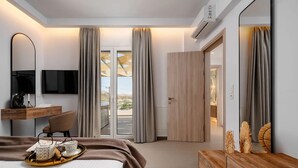 A modern hotel room with a bed, desk, TV, and a view through the glass door. - Thalelion Villa Private Pool and Jacuzzi (Naxos)