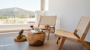 A room with two wicker chairs, a wooden stool, and a fruit basket by a window with a mountain view. - Thalelion Villa Private Pool and Jacuzzi (Naxos)