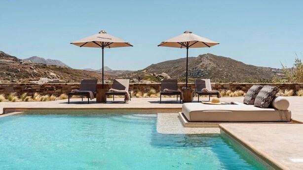 A pool area with lounge chairs and umbrellas, a sofa with cushions, and a mountainous backdrop. - Thalelion Villa Private Pool and Jacuzzi (Naxos)