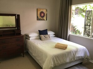 Une chambre à coucher avec un lit, une commode, un tableau et une fenêtre avec des rideaux.