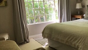 Un dormitorio con un ventanal grande, una cama, una mesita de noche con lámpara y una silla.