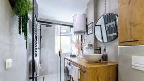 A modern bathroom with a glass shower enclosure, a wooden vanity, a large mirror, and a built-in washing machine. - Home Abroad (Zagreb)