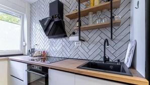 A modern kitchen with a herringbone tile backsplash, a black range hood, and a wooden countertop. - Home Abroad (Zagreb)