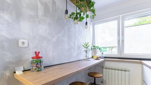 A kitchen with a wooden countertop, two stools, hanging plants, and a window with blinds. - Home Abroad (Zagreb)