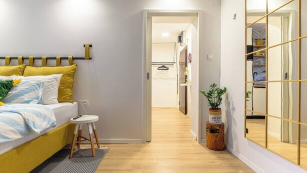 A modern bedroom with a bed, bedside table, and a mirror with a geometric frame. - Home Abroad (Zagreb)