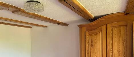 Ein hölzernes Bett mit Blumenmuster auf der Bettwäsche, ein Holzschrank und eine strukturierte Decke.