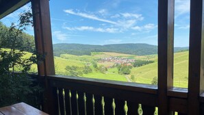 A wooden deck with a view of a green valley, a wind turbine, and a small village.