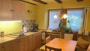 Una cocina con armarios de madera, cafetera, hervidor y zona de comedor con mesa y sillas.