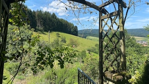 Una estructura de pérgola de madera con vistas a un paisaje verde, incluyendo colinas y un pueblo lejano.