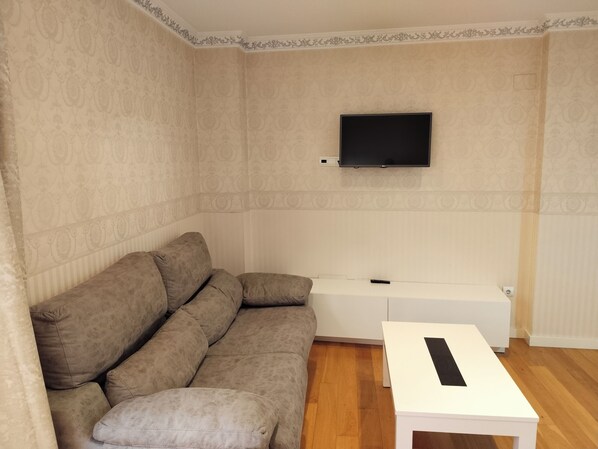 Una sala de estar con un sofá, una mesa de centro blanca y un televisor de pantalla plana montado en la pared.