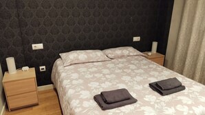 A neatly made bed with floral bedding, two bedside tables with lamps, and a power outlet on the wall.