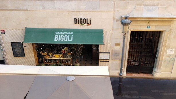 A restaurant named 'Bigoli' with a green awning, a visible outdoor seating area, and a building entrance with a number '6' above it.