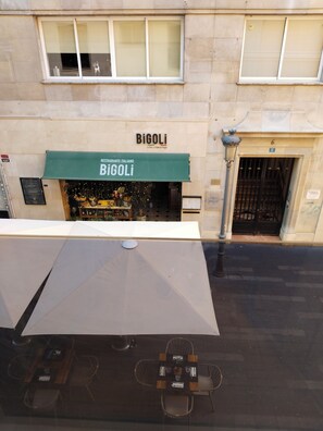 Un restaurante llamado 'Bigoli' con un toldo verde, una zona de mesas al aire libre visible y la entrada del edificio con el número '6' encima.