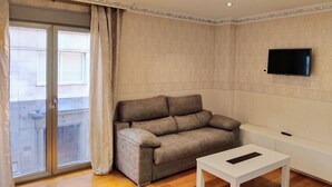 A living room with a sofa, a TV mounted on the wall, a sliding glass door, and a white table.